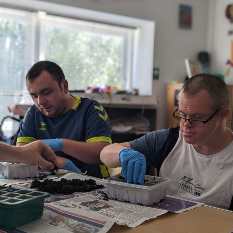 Two gentlemen plant seeds at a table