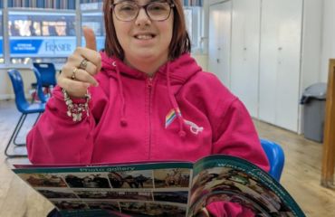 Amy holding a newsletter with her thumb up