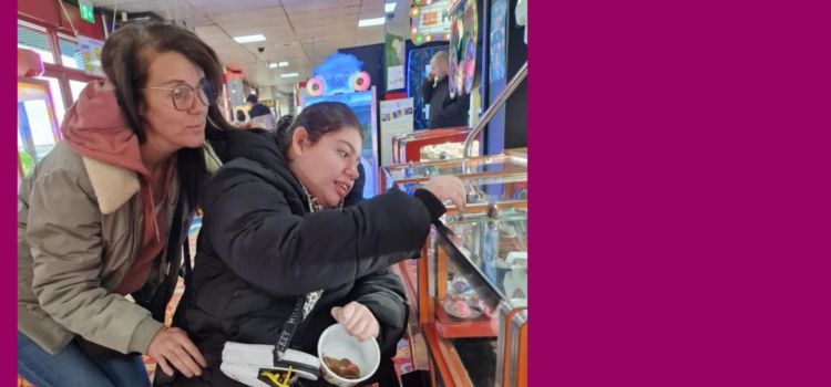 Two ladies at an arcade, one in a wheelchair with a money pot