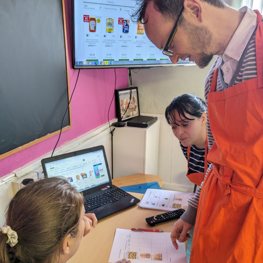 Two women and one man at a desk during the Living Skills course looking at the cost of ingredients