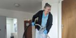 A female cleaner is smiling and hoovering