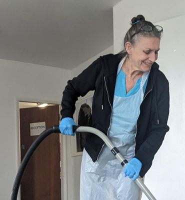 A female cleaner is smiling and hoovering