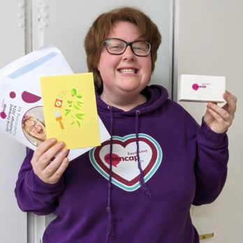 Natasha is smiling and holding up a fundraising kit