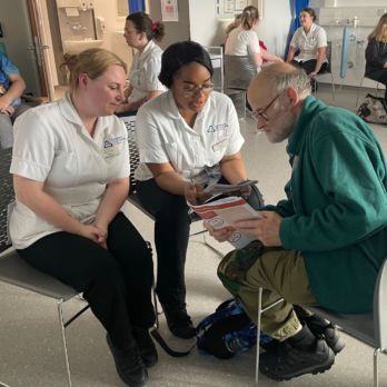 Man from GOLD showing a leaflet to two student nurses