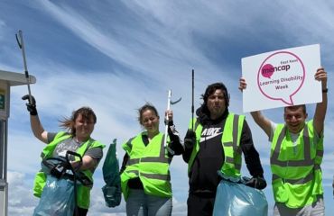 Four people wearing high vis jackets and holding litter picks and a Learning Disability Week sign
