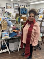 Rosie, a member with a learning disability, standing in front of her handmade hats in an Art Gallery in Westgate.