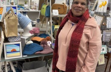 Rosie, a member with a learning disability, standing in front of her handmade hats in an Art Gallery in Westgate.