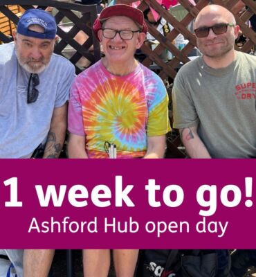 Three men sit together on a bench in the sunshine, smiling. They wear casual hats and sunglasses, and sit in front of a garden trellis. A purple banner over the photo reads: “1 week to go! Ashford Hub Open Day.”